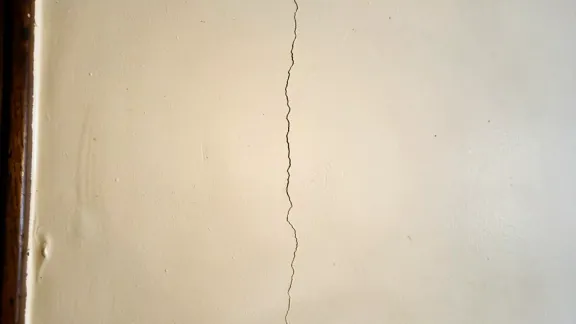 A fine vertical hairline crack running up a cream painted interior wall beside a narrow dark-wood door casing