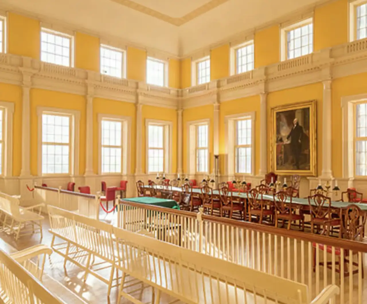 Historic Connecticut state government chamber with tall windows, columned plaster-finished walls, a portrait, and a spectator gallery above rows of desks