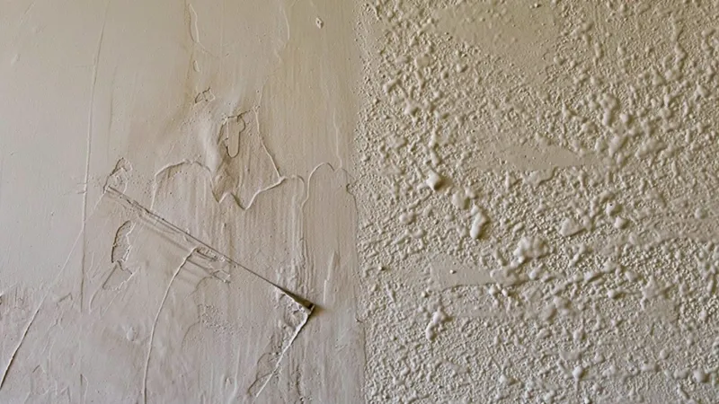 Freshly troweled joint compound on one half of a wall meeting a splatter knockdown texture on the other
